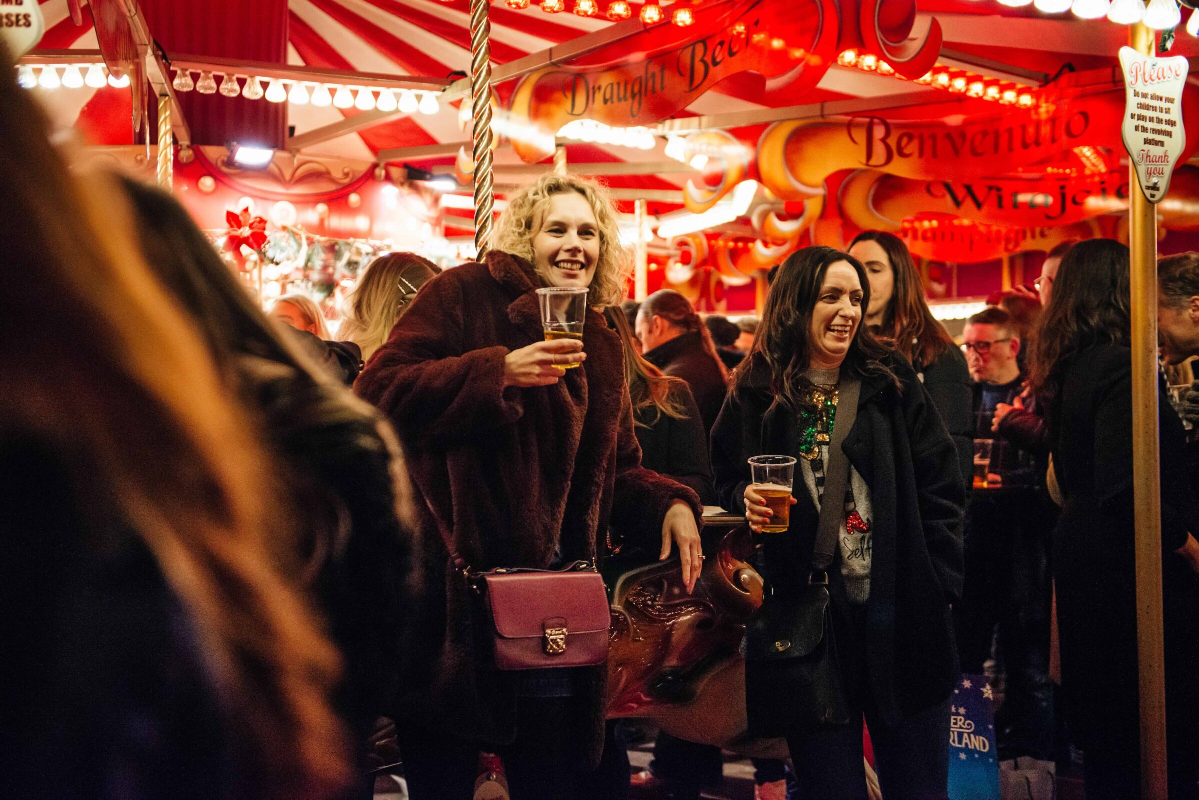 Friends enjoy drinks at the lively, warmly lit carnival-style Carousel Bar. Red and white striped decor surrounds them, creating a festive atmosphere.