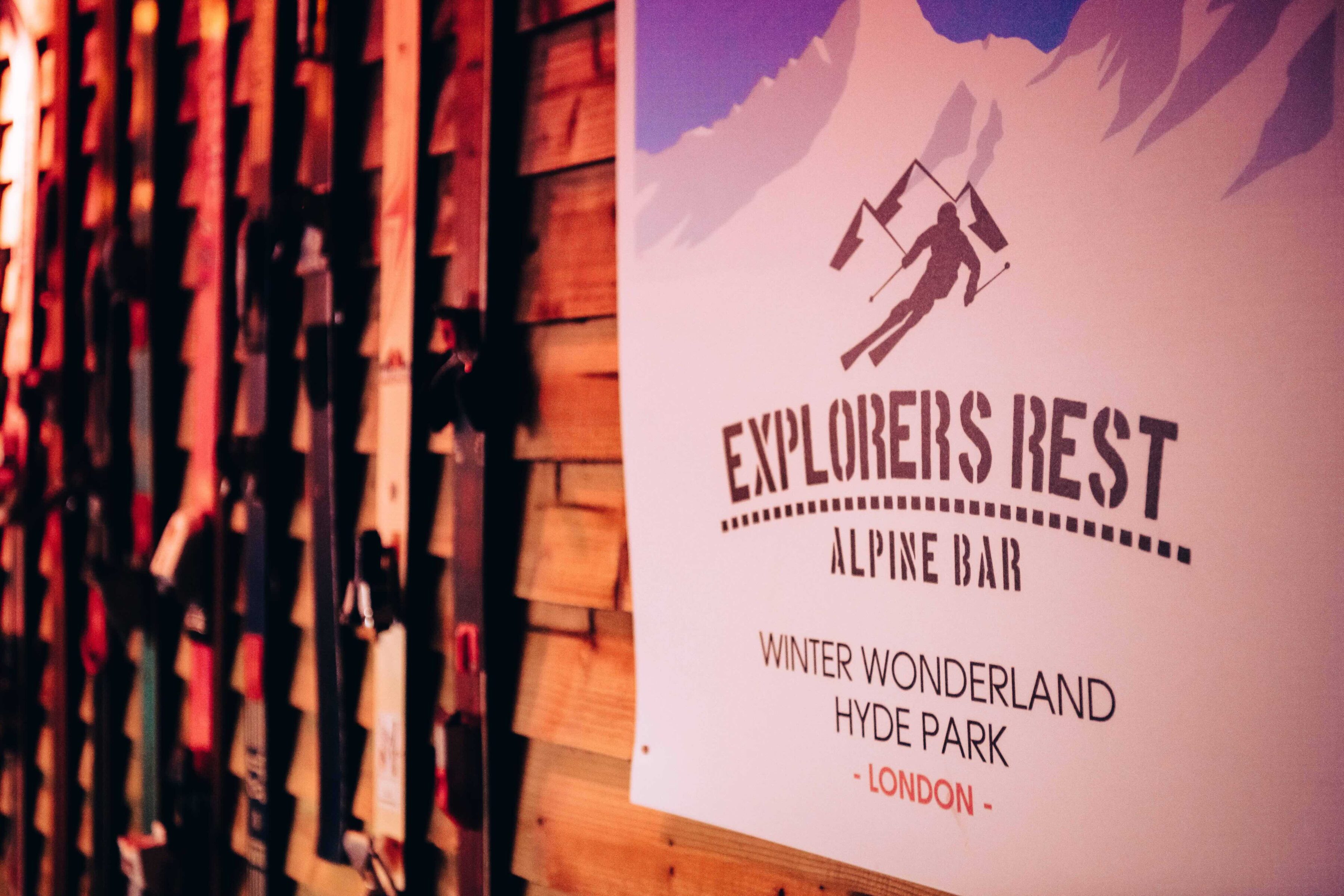 Poster for "Explorers Rest Alpine Bar" at Winter Wonderland, Hyde Park, London, featuring a skier. Warm wooden backdrop suggests a cozy alpine theme.