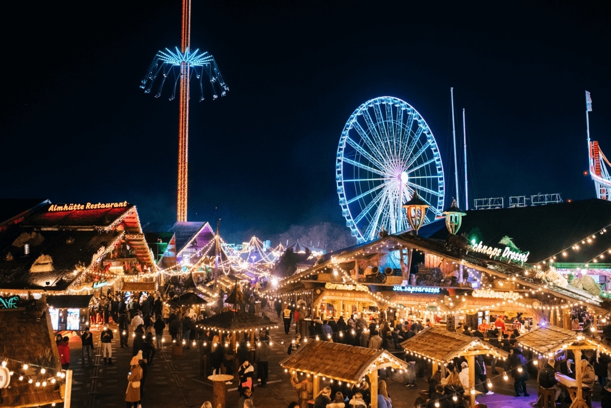 Festive night market scene at Hyde Park Winter Wonderland with glowing stalls, a towering Ferris wheel, and a brightly lit swing ride. Crowds enjoy a cheerful, lively atmosphere.