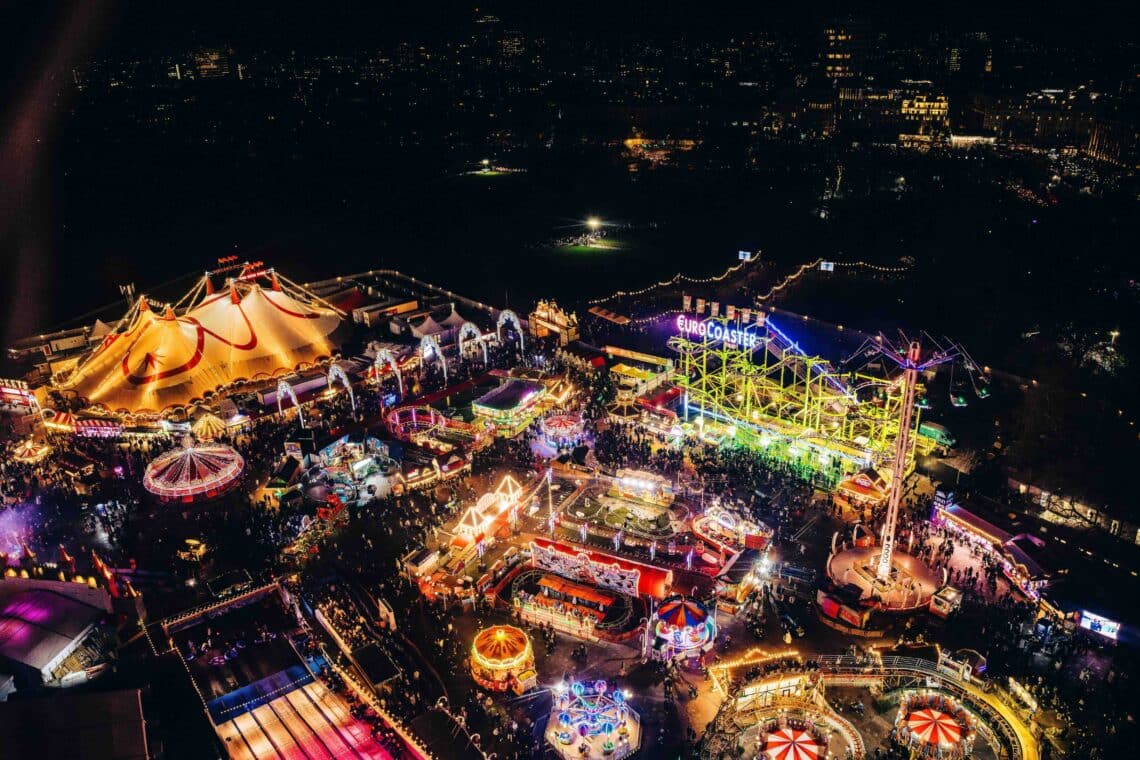 A vibrant aerial view of Hyde Park Winter Wonderland, featuring colourful rides, a lit-up Euro Coaster, and lively crowds enjoying the festive atmosphere.