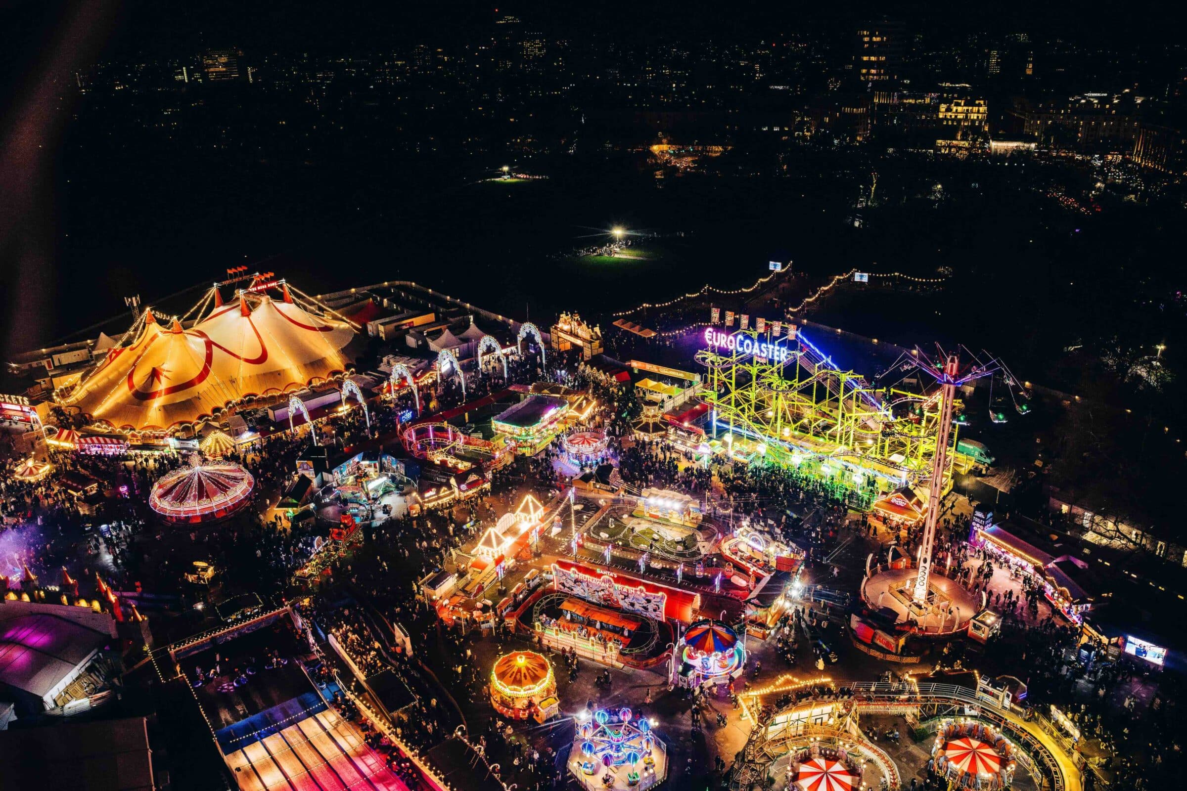 A vibrant aerial view of Hyde Park Winter Wonderland, featuring colourful rides, a lit-up Euro Coaster, and lively crowds enjoying the festive atmosphere.