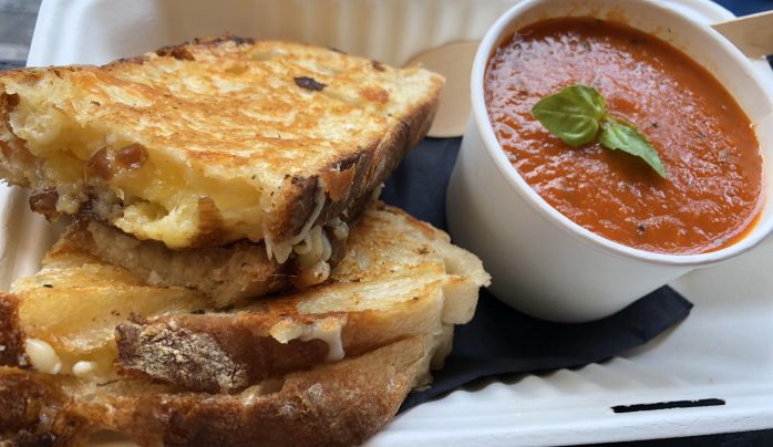 A crispy grilled cheese sandwich stacked in a tray beside a cup of rich tomato soup garnished with fresh basil, creating a warm, comforting vibe.