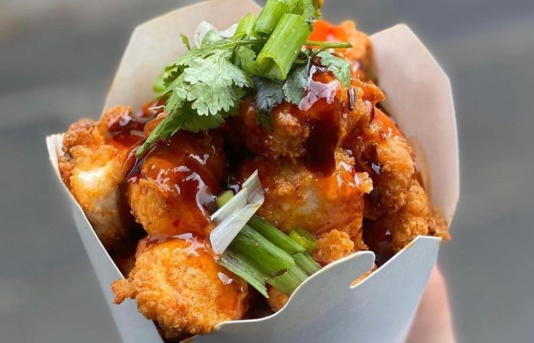Crispy fried chicken bites in a paper cup, topped with glossy sauce, garnished with fresh cilantro and green onions, creating a savoury, appetising look.