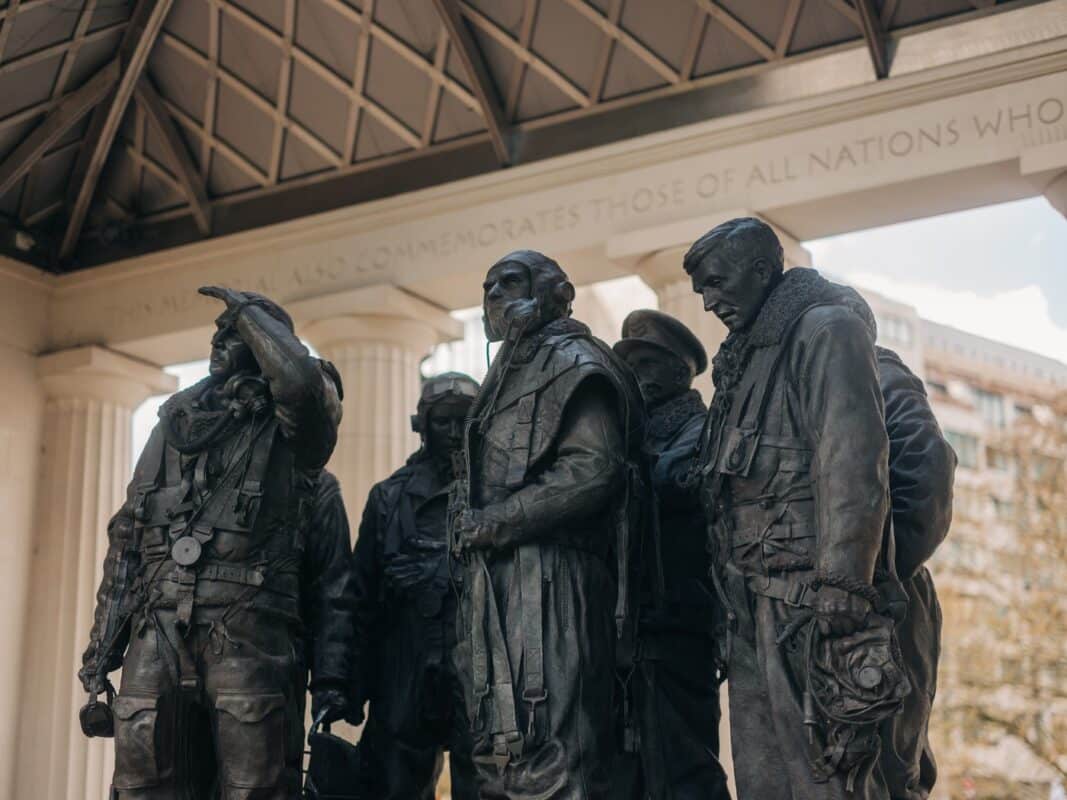 Bronze statues of airmen in WWII attire stand solemnly under a pavilion, symbolising remembrance and honour. An inscription is partially visible above.
