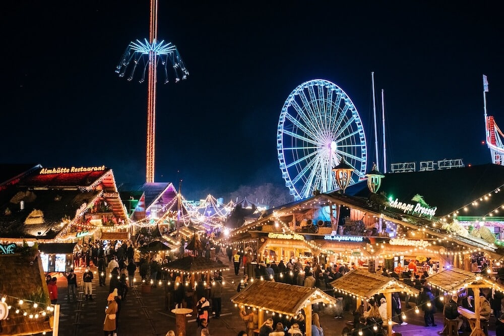 Nighttime amusement park scene with a large, illuminated Ferris wheel in the background.