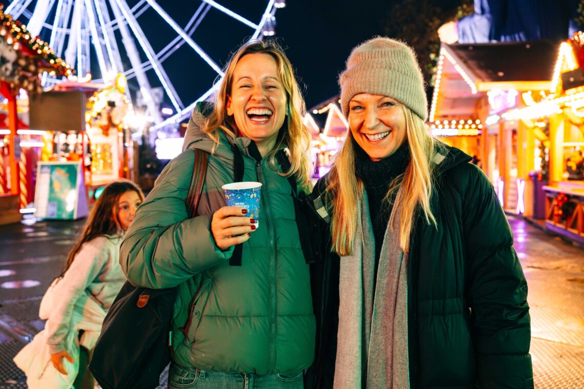 Two women laughing and holding a hot drink as the walk through Winter Wonderland