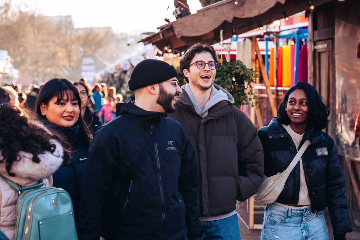 Group of four young people walking through Winter Wonderland, laughing and smiling